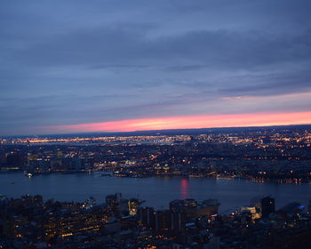 Aerial view of river amidst illuminated cityscape during sunset