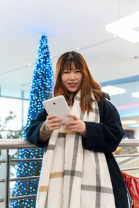 Young pretty woman of chinese ethnicity while typing a tablet in front of blue christmas tree indoor