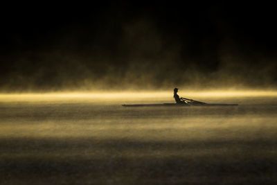 Silhouette person rowing on a lake at dawn