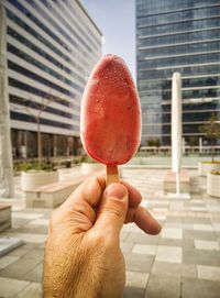Close-up of hand holding popsicle against modern buildings in city