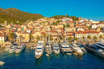 Sailboats moored in harbor by town against clear blue sky