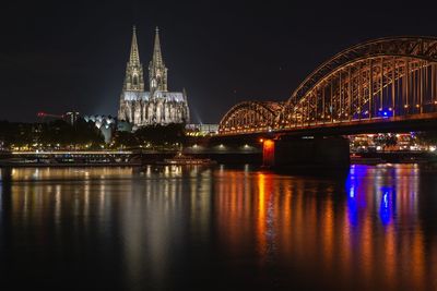 Illuminated bridge over river against cologne cathedral at night