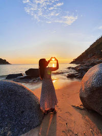 Woman standing on rock at beach against sky during sunset