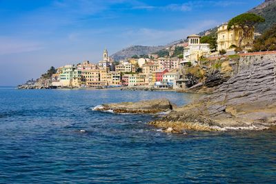 Buildings by sea against blue sky