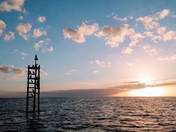 Silhouette tower by sea against sky during sunset