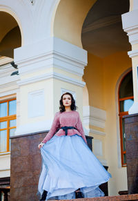 Portrait of young woman standing against built structure