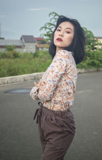 Young woman looking away while standing on road in city