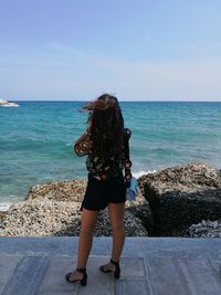 Rear view of woman standing by sea against clear sky