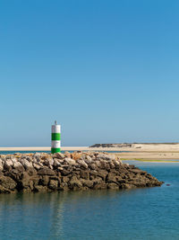 Lighthouse by sea against clear blue sky