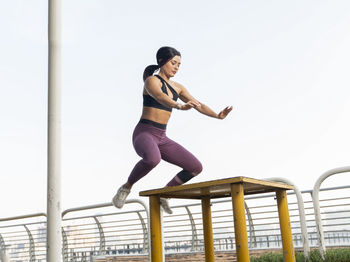 Full length of woman sitting on railing against sky