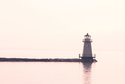 Lighthouse by sea against clear sky