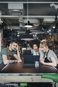 Male and female mechanics using laptop at table in workshop