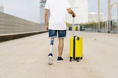Disabled young man walking with luggage at sidewalk in city