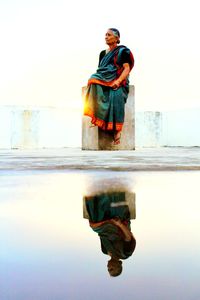 Reflection of woman in puddle against clear sky during sunset