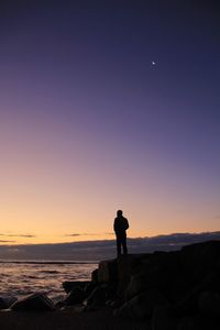 Silhouette man standing on rock by sea against sky during sunset