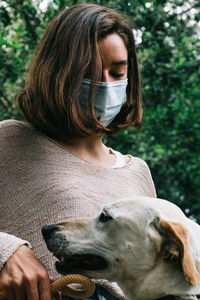 Young woman wearing a face mask caressing a dog playing in the park. concept of new normal outdoors.