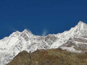 Low angle view of snowcapped mountain against blue sky