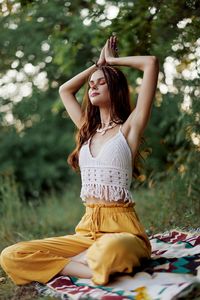 Young woman looking away while sitting against trees