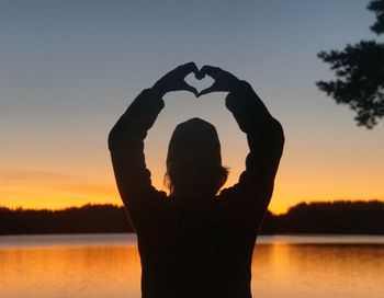 Silhouette woman standing by heart shape on lake against sky during sunset