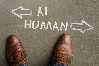 Man looking down at the words artificial intelligence - ai - and human chalked onto the floor