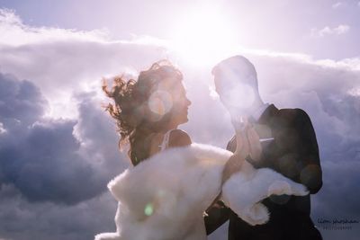 Low angle view of couple kissing against cloudy sky