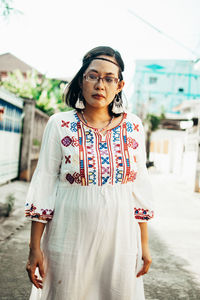 Portrait of young woman standing against building