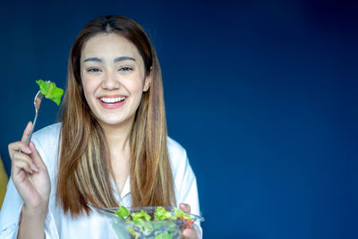 Portrait of smiling young woman holding flowers against blue background