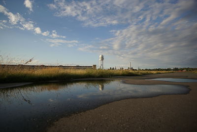 Reflection of tall structure seen in water with grass in foreground