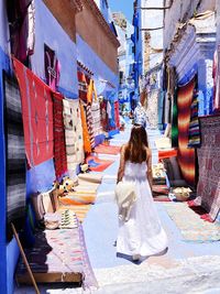 Rear view of woman walking amidst colorful shawls at alley in city