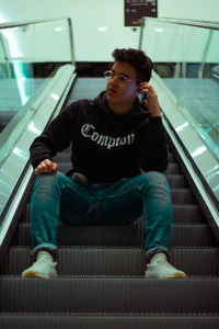 Full length of man using mobile phone while sitting on escalator