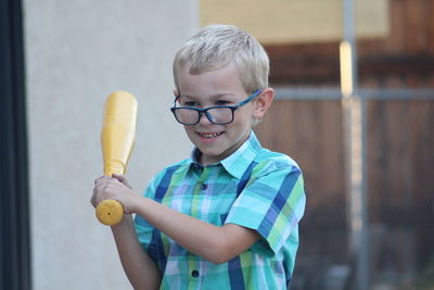 Cute smiling boy holding baseball bat while standing outdoors