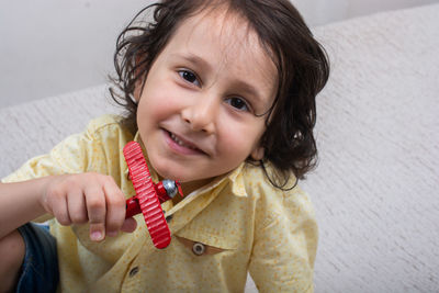 Portrait of smiling boy holding toy while sitting on seat at home