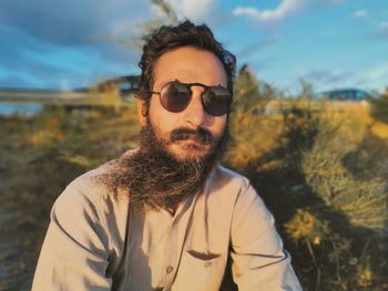 Portrait of young man wearing sunglasses against lake