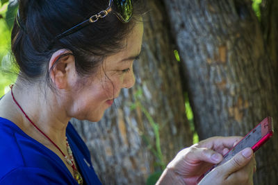 Close-up of senior woman using smart phone by tree