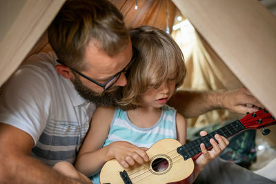 Portrait of a 6 year old boy and his father having fun playing guitar in teepee tent.