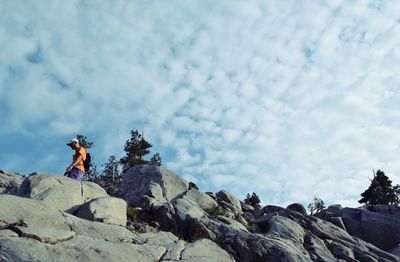 Low angle view of man standing on rock against cloudy sky