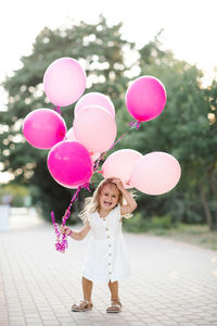 Funny laughing kid girl 3-4 year old holding pink balloons wear white dress outdoor over nature