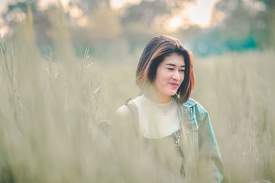 Smiling thoughtful young woman looking away while standing on grassy field