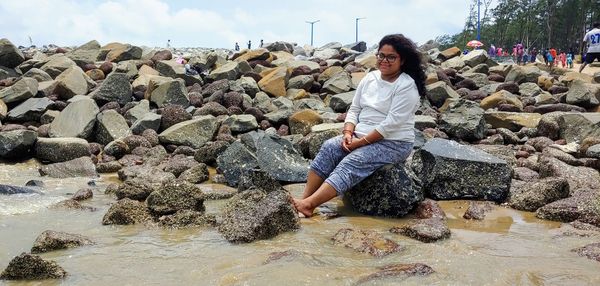 Full length portrait of young woman standing by rocks