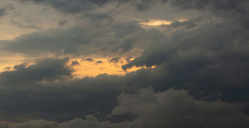 Low angle view of sunlight streaming through clouds during sunset