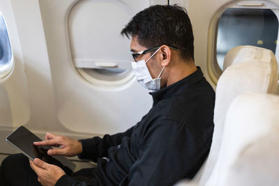 Side view of man using tablet pc in plane during pandemic