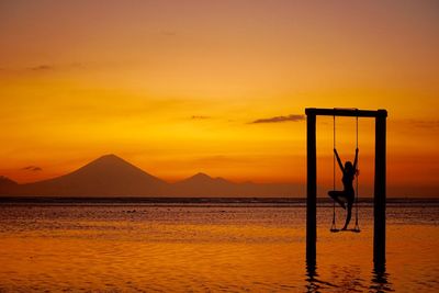 Silhouette woman on swing over sea against sky during sunset