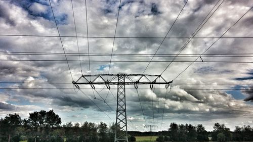 Low angle view of electricity pylon against cloudy sky