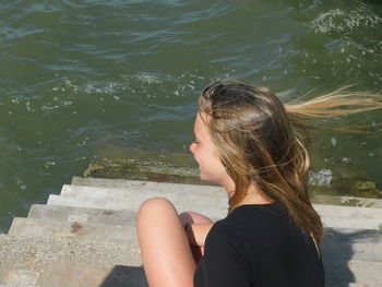 High angle view of young woman sitting on steps by sea