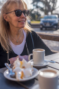 Mature adult woman smiling wearing glasses with a latte and lemon pie. looking away