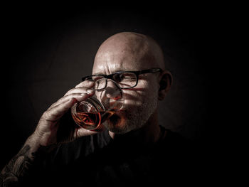 Portrait of man holding eyeglasses against black background