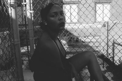 Portrait of young woman looking through chainlink fence