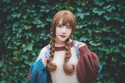 Portrait of young woman with braided hair standing against plants at park