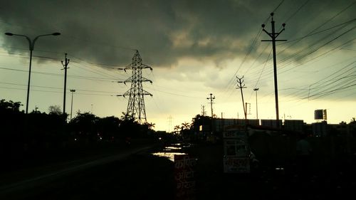 Electricity pylon against cloudy sky at sunset