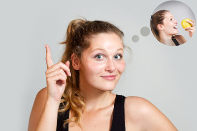 Digital composite image of smiling young woman pointing upwards with thought bubble against gray background